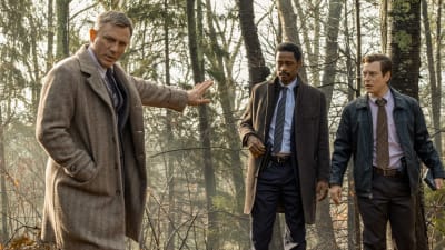 Benoit Blanc (Daniel Craig) står i skogen tillsammans med poliserna Elliott (LaKeith Stanfield) och Trooper Wagner (Noah Segan) och försöker kolla fotspår i leran.