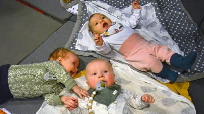 Tre små bebisar ligger på filtar på golvet. 