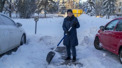 Raija Pitkänen gräver fram sin parkeringsplats med en spade.