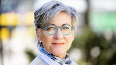 En gråhårig kvinna med blåa runda glasögon.