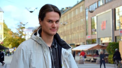 en man i grå jacka står vid gågatan i Åbo där människor går och cyklar omkring