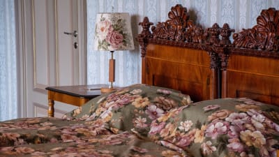 Två sängar i gammaldags stil i sovrummet, bäddat med blommigt överkast. BLommig lampa står på nattduksbordet.