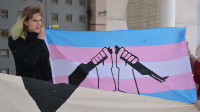 Elsa Tauria håller i en blå, rosa och vit banderoll med en bild av ett svart vapen som bryts i två delar. 