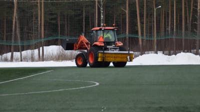 En traktor kör bort snö från sidorna av den uppvärmda konstgräsplanen i Karis den 6 mars 2018.