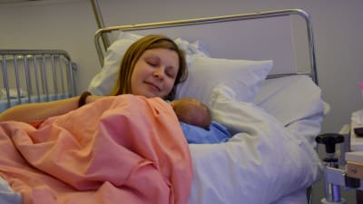 Anna Ahlnäs ligger i en sjukhussäng med sin nyfödda dotter i famnen. 