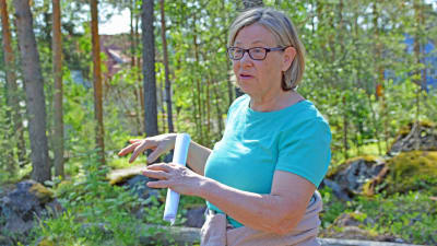 Kvinna står och förklarar något med händerna i en tallskog.