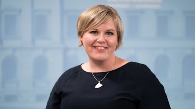 Annika Saarikko poserar mot  en blå bakgrund. 