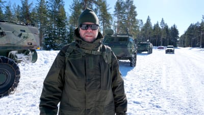Man i solglasögon står framför en rad militärfordon.