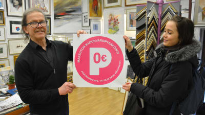 Rainer Lindewall och Hilla Inki håller upp en skylt med röd text: Parkering 0 euro.