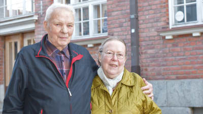 Ett äldre par, kvinna och man, står ute vid Ekenäs gågata och håller om varandra.
