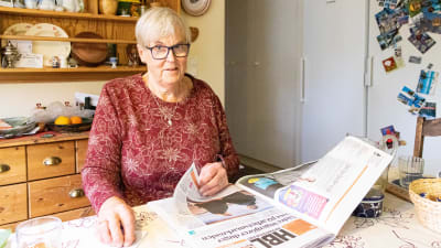En kvinna som läser tidningen vid köksbordet.