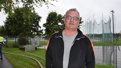 Arbetsledare Ronnie Westerlund med den översvämmade idrottsplanen i bakgrunden.