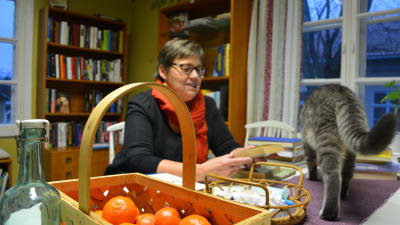 Kvinna sitter och bläddrar i en bok vid ett bord med mandariner och en katt. 