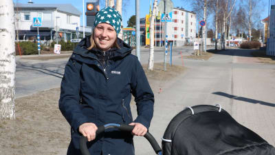 En ung kvinna med barnvagn står på en gata.