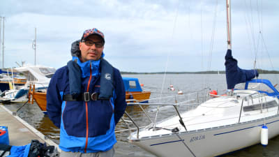 En man i seglarklädsel framför en segelbåt