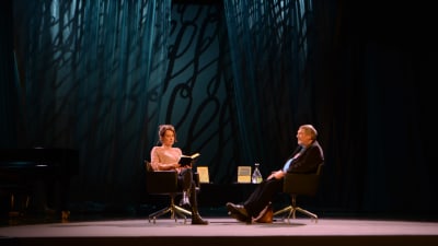 En man och en kvinna sitter i fåtöljer på en scen.
