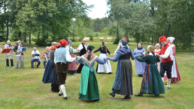 Människor i folkdräkt dansar folkdans i en park.