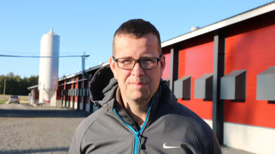 En man med kort mörkt hår och glasögon står framför en stor kalkonhall.