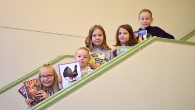 Fem barn i tioårsådern står i en trappa med böcker i händerna.