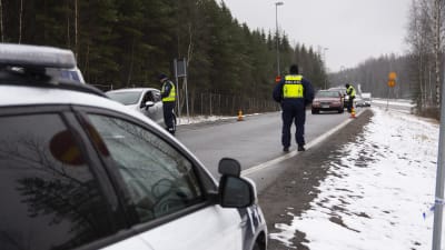 En landsväg med flera bilar som stannat och poliser i gula västar. Det finns lite snö på marken. Polisen övervakar den nyländska landsskapsgränsen.