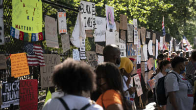 Människor och plakat vid staketet runt Vita huset i Washington.