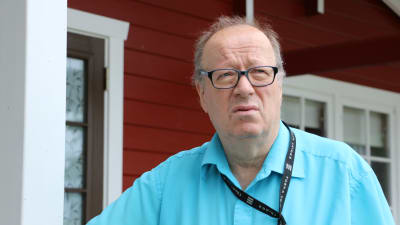 En skallig medelålders man med ljusblå pikéskjorta lutar mot ett räcke och ser bekymrad ut.