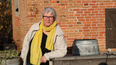 En kvinna i halsduk och glasögon framför en tegelvägg. 