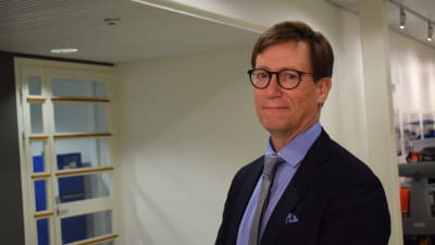 En man i kostym och glasögon ler mot kameran.