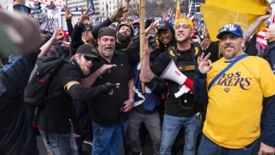 Män i svarta och gula tröjor poserar för kameran. En person har en megafon, en annan en gul och blå flagga. De står mitt i en demonstation.