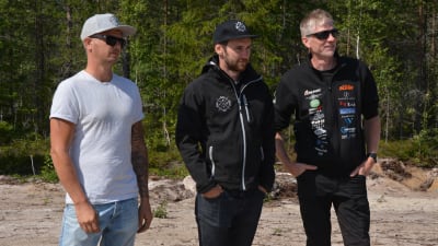 Tre män står och tittar på en motocross.
