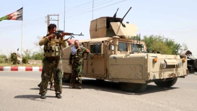Två soldater står framför ett pansarfordon.  I bakgrunden vajar Afghanistans flagga