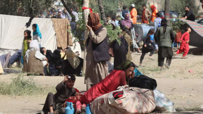 En flyktingfamilj sitter bredvid sina ägodelar. I bakgrunden syns några enkla tält.