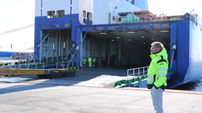 En man står vid kajen och följer med då ett fraktfartyg lastas.