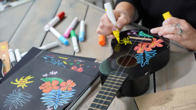 Närbild av händer som ritar med penna på en ukulele.