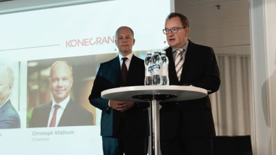 Två medelåldersmän iklädda kostym. De ger en presentation av fusionen mellan bolagen Konecranes och Cargotec.