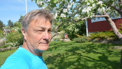 En man i en blå t-skjorta står i en trädgård med blommande äppelträd