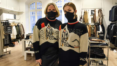Två kvinnor i likadana stickade tröjor och munskydd står inne i en klädbutik.