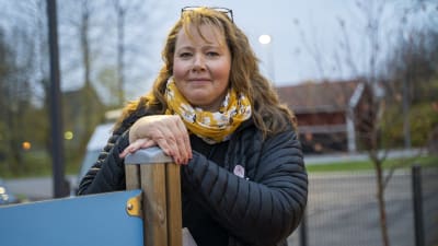 En kvinna står ute på gården vid ett daghem, daghemmet Karusellen i Karis. Hon lutar sig mot en stolpe till en klätterställning.