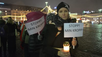 Kvinna håller plakat med texten stopp min kropp och ett tänt ljus under me too- demonstration i Åbo. 