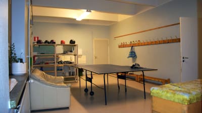 En trång aula i en skola där en beige lädersoffa står invid ett pingisbord. Till höger syns en vit dörr som står öppen.