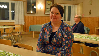 En kvinna sitter vid ett bord inne i en föreningssal.