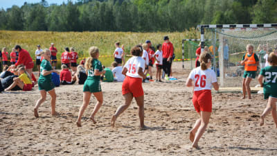 Två handbollslag spelar handboll på en strand.