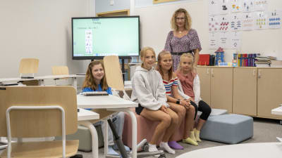 Fyra elever sitter och en lärare står i ett klassrum.