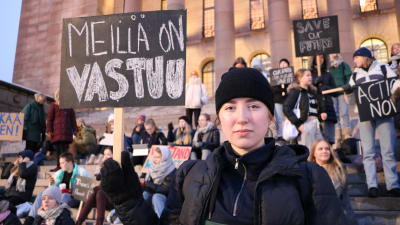 Den svartklädda Ilon Adlercreutz har en skylt med texten "Meillä on vastuu" (Vi har ett ansvar). 