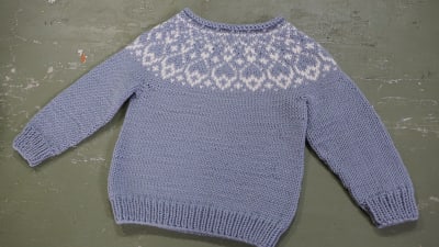 En stickad tröja för en ettåring med mönster i oket.