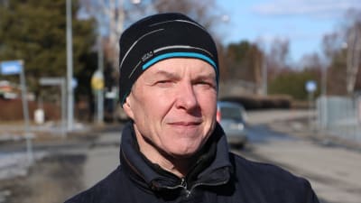 En man med mössa på huvudet står intill en väg.