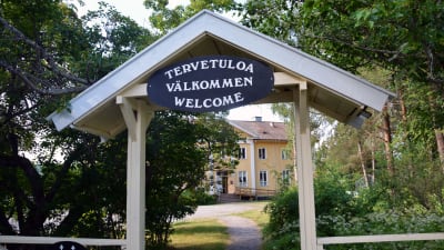 En skylt med texten "välkommen" på tre olika språk framför Sagalunds byggnad.