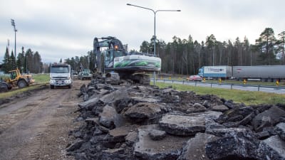 En grävmaskin lastar uppbruten asfalt på en lastbil.