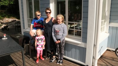 Rosa Pentikäinen-Mattila står med sina barn i solskenet ute på terassen och tittar mot kameran.
