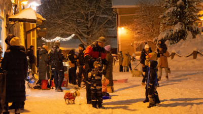 Många människor på Gamla Rådhustorget i snöyran. En liten pojke håller i en pappmugg och pekar på något. Flera hundar, barn och pulkor syns i bild.